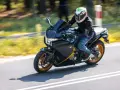 Motocyklista w kasku z uśmiechniętą twarzą pędzi na czarnym motocyklu Honda VFR 1200 po drodze.