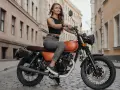Kobieta w czarnym topie i jeansach siedzi na pomarańczowym motocyklu na brukowanej ulicy. To idealna kategoria a dla miłośniczek wolności.