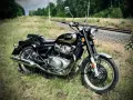 Czarny Royal Enfield Classic 650 lśni chromem na tle torów kolejowych i zieleni. Gotowy na przygodę.