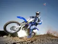Motocyklista na Yamasze 125 w powietrzu, unosząc się nad ziemią. W tle błękitne niebo.