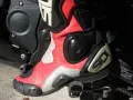 Czerwono-biały but motocyklowy Sidi obok dźwigni zmiany biegów w motocyklu. Gotowy do jazdy.