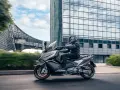 Mężczyzna w kasku jedzie na skuterze Kymco AK 550 obok nowoczesnego budynku.