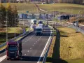 Ciężarówki na Via Baltica w jesiennym krajobrazie. Droga szybkiego ruchu z wieloma pojazdami, w tym czerwonym Scanią.