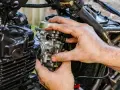 Dłonie mechanika regulują gaźnik motocykla, kluczowy element odpowiedzialny za symbol ssania paliwa i powietrza.