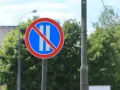 Znak B37 zakazujący postoju. Dwa pionowe białe paski na niebieskim tle, przekreślone czerwoną linią.