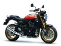 Stylowy czarny motocykl Kawasaki Z900RS z pomarańczowo-żółtym malowaniem na baku i złotymi felgami.