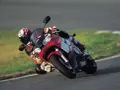 Motocyklista na torze pochyla się na swoim czerwono-białym motocyklu Yamaha R6 2001, w pełni ubrany w kombinezon i kask.