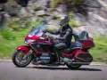 Mężczyzna w kasku i kombinezonie jedzie na czerwonym motocyklu honda turystyk. W tle rozmyte zielone wzgórza i skały.