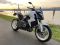 Biały motocykl Honda CB1000R, model a2 motor, zaparkowany nad rzeką o zachodzie słońca.