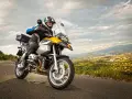 Motocyklista w kasku jedzie na motocyklu turystycznym. W tle rozciąga się malowniczy krajobraz z miastem. Zastanawiasz się nad koszt przerejestrowania motocykla?