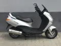 Srebrny skuter Peugeot Elyseo 125 z czarnym siedzeniem i przyciemnianą szybą, zaparkowany na chodniku.