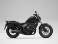 Czarny motocykl Honda Rebel 500 z sakwami, gotowy na podróż. Jego prędkość maksymalna pozwala na swobodne pokonywanie tras.