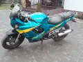 Turkusowy Suzuki GSXF 600 z żółto-fioletowymi grafikami, zaparkowany na kostce brukowej przed domem.