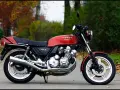 Klasyczny motocykl Honda CBX 1000 w kolorze czerwonym, z widocznym potężnym silnikiem i chromowanymi elementami, zaparkowany na tle jesiennej zieleni.