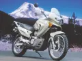Srebrny motocykl Honda Transalp 650 gotowy na przygodę na tle ośnieżonej góry i lasu.