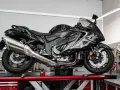 Czarny, lśniący motocykl typu naked bike na podnośniku w warsztacie. W tle tablica z narzędziami i napis "NAPRAWA".