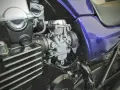 Szczegółowy widok gaźnika motocyklowego, kluczowego elementu układu dolotowego, z widocznymi przewodami i częściami silnika.