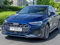 Młody kierowca w czapce za kierownicą granatowego Audi A3, jadącego po miejskiej drodze.