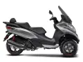 Srebrny Piaggio MP3 500, trójkołowy skuter z czarnym siedzeniem i dużą szybą. Poznaj jego piaggio mp3 500 dane techniczne.