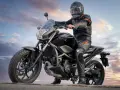 Motocyklista w kasku i kombinezonie siedzi na czarnym motocyklu. Idealny motor na kat B, gotowy na przygodę.