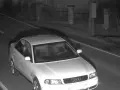 Biały sedan Audi przejeżdża przez nocne zdjęcie z fotoradaru.