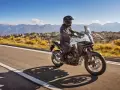Motocyklista na białym Honda CB500X przemierza malowniczą, górską drogę.