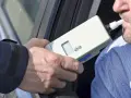 Badanie alkomatem. Kierowca dmucha, by sprawdzić, na ile zabierają prawo jazdy za alkohol 1 promil.