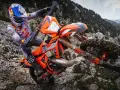 Motocyklista w kasku Red Bull na pomarańczowym KTM EXC 300 2T pokonuje kamienisty teren. Dane techniczne tego potwora terenowego są imponujące.