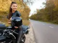Uśmiechnięta kobieta w skórzanym stroju trzyma kask obok swojego motocykla. Idealne motory dla kobiet na jesienną przejażdżkę.