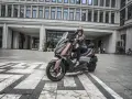 Kobieta na skuterze Yamaha X-MAX 300, gotowa do jazdy. Zastanawia się, jaka będzie jej prędkość maksymalna w mieście.
