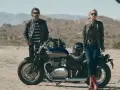 Para w skórzanych kurtkach pozuje przy motocyklu Triumph Speedmaster na pustynnym tle.