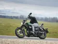 Motocyklista na zielonym chopperze UM Renegade 125 przemierza malowniczą drogę wśród zielonych pól i gór.