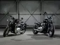 Dwa motocykle Triumph Bonneville Bobber w ciemnych kolorach, stojące obok siebie w industrialnym wnętrzu.