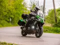 Motocyklista na zielonym Kawasaki Versys 1000, z kuframi, pokonuje zakręt. Nawet z potencjalnymi wadami, jazda nim to przygoda.