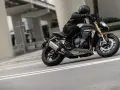 Motocyklista w kasku i skórzanej kurtce pochyla się na swoim motocyklu Triumph Speed Triple, pokonując zakręt na miejskiej drodze.