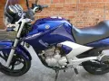 Błękitny motocykl Yamaha YBR 250 z chromowanymi elementami, zaparkowany na tle ceglanej ściany.