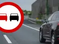 Znak P3 zakazujący wyprzedzania. Czerwony i czarny samochód na drodze.