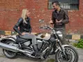 Kobieta siedzi na motocyklu Yamaha Warrior 1700, mężczyzna obok opowiada o jego możliwościach.