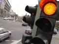 Żółte światło na sygnalizatorze drogowym, ruch uliczny i budynki w tle.