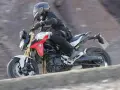 Motocyklista w kasku i kombinezonie pędzi na motocyklu BMW F900R po kamienistym terenie.