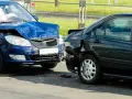 Dwa uszkodzone samochody po kolizji. Niebieski przód jest mocno zgnieciony, a czarny tył również nosi ślady uderzenia. Prawdopodobnie czeka ich mandat za kolizje.