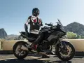 Motocyklista w kombinezonie na czarnym motocyklu BMW, gotowy do podróży po górskich drogach. Wśród wielu marek motocykli, ta prezentuje się imponująco.