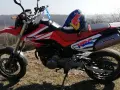 Czerwony motocykl Honda FMX 650 z kaskiem Red Bull na siedzeniu, gotowy na przygodę w terenie.