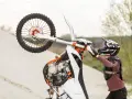Motocyklista w kasku i ochraniaczach wykonuje wheelie na piaskowej wydmie. To najszybszy cross na świecie, gotowy do akcji.