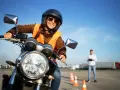 Uśmiechnięta kursantka w kamizelce odblaskowej i kasku na motocyklu, przygotowuje się do egzaminu na prawo jazdy A2.