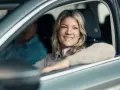 Uśmiechnięta kobieta za kierownicą, zastanawia się, czy można płacić kartą na autostradzie. Obok siedzi pasażer.