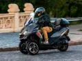 Mężczyzna w kasku jedzie trójkołowym skuterem Peugeot Metropolis 400. Widoczna jest jego prędkość maksymalna.