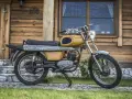 Żółty motorower WSK 175, z widocznymi danymi technicznymi na silniku, stoi przed drewnianym domem.