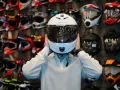 Osoba przymierza biały, cichy kask motocyklowy Schuberth. W tle widać ścianę pełną kolorowych kasków.