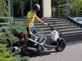 Młody mężczyzna w kasku i żółtej koszulce przy białym skuterze. To jego stara karta motorowerowa, gotowa do jazdy.